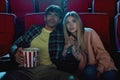 Focused young couple, attractive man and woman sitting at the cinema, watching a movie with enthusiasm and holding hands