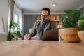 Focused young elegant businessman signing documents while working over laptop on desk at home office Royalty Free Stock Photo