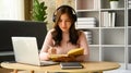Focused young female student wearing headphones listening online lecture and making notes on notebook Royalty Free Stock Photo