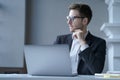 Focused young German male office worker sits at desk at home workplace distracted from laptop screen