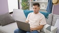 Focused young hispanic man, engrossed in his laptop while working online, sitting, on a cozy sofa at home in a well-illuminated Royalty Free Stock Photo