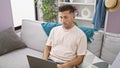 Focused young hispanic man, engrossed in his laptop while working online, sitting, on a cozy sofa at home in a well-illuminated Royalty Free Stock Photo