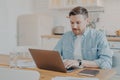 Focused young man freelancer using laptop while sitting at kitchen table Royalty Free Stock Photo