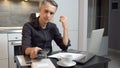 Focused young man working on laptop and using smartphone while sitting in kitchen at home Royalty Free Stock Photo