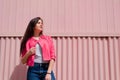 Focused young woman with long straight dark hair in white t-shirt, leather jacket and blue jeans on pink background. Female Royalty Free Stock Photo