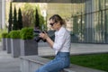 Focused young woman sitting on bench in spring park under tree outdoors resting using camera Royalty Free Stock Photo