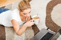 Focused young woman using laptop while lying on floor and drinking coffee Royalty Free Stock Photo