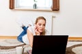 Focused young woman using laptop while lying on floor and drinking coffee Royalty Free Stock Photo