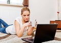 Focused young woman using laptop while lying on floor and drinking coffee Royalty Free Stock Photo