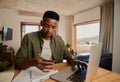 Focussed young adult black male making online payment on laptop in modern apartment. Royalty Free Stock Photo