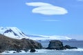 Foehn cloud over landscape with lots of penguins on rocks and snowcapped mountains in background, Antarctica Royalty Free Stock Photo
