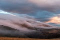 Fog covering some mountains and trees, with warm sunset colors