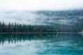 Fog hangs over a lake with evergreen trees reflected in the still water Royalty Free Stock Photo