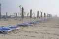 Foggy beach with blurred rows of closed parasols and sun bed in off-season on misty day.Thick fog on the beach area Royalty Free Stock Photo