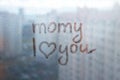 Foggy glass on window with written finger word momy i love you with heart shape on blue overcast wet window