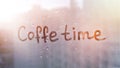 Foggy glass on window with written finger words coffe time on muddy blue glass wet orange window in city on sunset