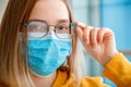 Foggy glasses wearing on young woman. close up portrait. Teenager girl in blue medical protective face mask and eyeglasses wipes Royalty Free Stock Photo