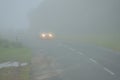 Foggy landscape of road and car moving with headlights turned on. Densely mist in the winter by clouds