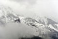 A foggy misteric panoramic view of the Alps mountains partially covered with the snow on a cloudy October
