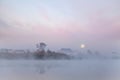 Foggy morning near the calm river, church reflected in calm water, full moon. Ukraine Royalty Free Stock Photo