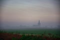 foggy morning with a view of wet fields and in front of the small Dutch village. Morning dew in the countryside.