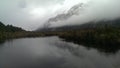 Foggy mystic morning on a lake close to Milford Sound, snow capped mountain