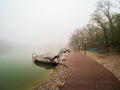 Foggy rainy autumn landscape with modern park in Zheleznovodsk with wooden pier and willow tree under lake. Caucasus region, Royalty Free Stock Photo