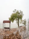 Foggy rainy landscape with modern park in Zheleznovodsk with wooden swinging bench and willow tree under lake. Caucasus region, Royalty Free Stock Photo