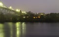 Foggy and Rainy Moody Night Landscape under Sagamore Bridge at Cape Cod Canal. Lighted Village and Yellow and Orange Light Reflect