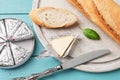 Foil wrapped processed cream cheese, table knife and slice of bread on a cutting board over blue wooden table. Small triangular