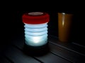 Fold up LED camping light and orange drinking mug standing on aluminium camping table in darkness, Travel, Africa