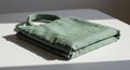 Folded green fabric bag on a white surface, highlighted by natural light and shadows. Royalty Free Stock Photo