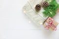 Folded knitted off-white wool sweater gift box pine cones green juniper twig golden lights garland on plank wood table. Christmas