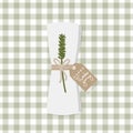 Folded napkin with twig, little bow and brown paper tag. Table set for Thanksgiving Day. Green checkered tablecloth background