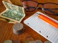 Folded One US dollar banknote, stack of coinsUS quarter dollar on the top, a notepad with a pen, glasses and a pile of coins in Royalty Free Stock Photo