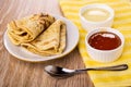 Folded pancakes on saucer, bowls with condensed milk, apricot jam on napkin, spoon on table Royalty Free Stock Photo