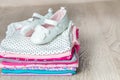 Folded pink and white bodysuit with shoes on it grey wooden background. diaper for newborn girl. Stack of infant clothing. Child