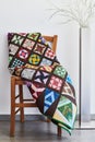 Folded quilt on a chair and floor lamp against a neutral wall