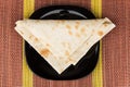 Folded triangle of thin Armenian lavash in black plate on mat