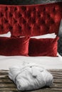 Folded white bathrobe on the bed against background of cushions and pillows red padded wall. Classic luxury style interior