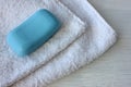 Folded white terry towel and blue soap on a white wooden table. Soft cotton bath towel background. Royalty Free Stock Photo