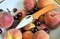 Folding knife stainless steel blade orange aluminum handle and fresh organic ripe fruits peach cherry natural gourmet product dess Royalty Free Stock Photo