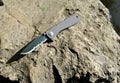 Folding knife stainless steel sharp blade gray handle close up still life stone background