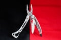 Folding multi tool with stainless steel sharp blade silver handle carabineer and screwdriver closeup still life black red backgrou