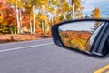 Foliage colors in fall season. Rural road in the autumn with yellow, brown and red colored trees reflected in car mirror Royalty Free Stock Photo