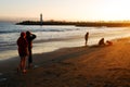 Folks walk and play at on a beach as the sun descends