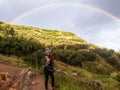 Follow your dream concept. A woman walking along the path to mountain and looking rainbow in the sky.