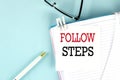 FOLLOW STEPS text on a sticky on notebook with pen and glasses , blue background Royalty Free Stock Photo