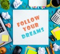Follow your dreams. Office table desk with supplies, white blank note pad, cup, pen, pc, crumpled paper, flower on blue Royalty Free Stock Photo