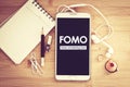 FOMO , Fear of missing out text on  Smart phone with a Blank notepad and  pencil  on wooden table Royalty Free Stock Photo